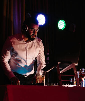 DJ im Anzug/Smart Casual an den Decks, Bühnenlicht.